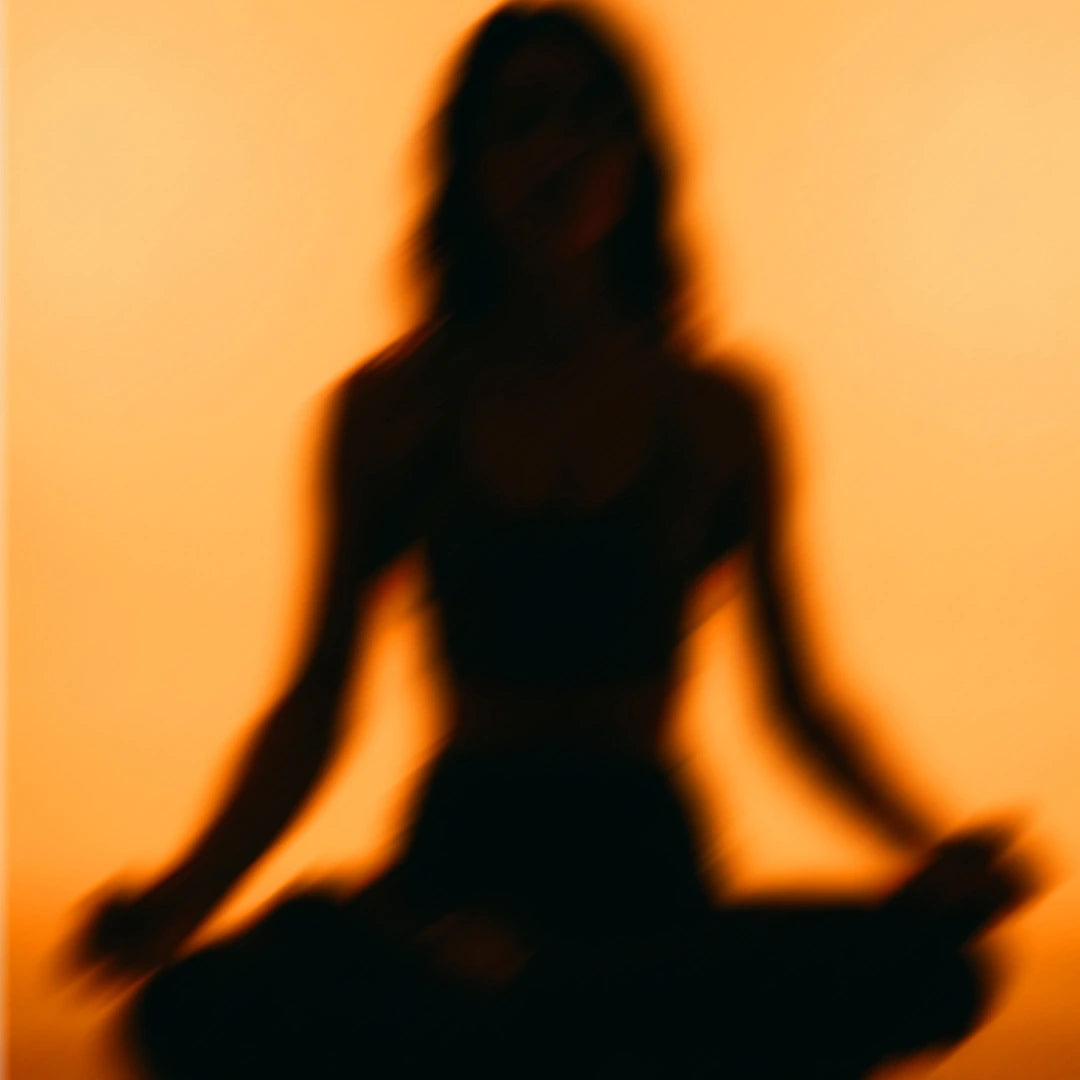 tark verschwommene, dunkle Silhouette einer Person, die im Meditationssitz (Schneidersitz) vor einem gleichmäßig hellorange leuchtenden Hintergrund verweilt.