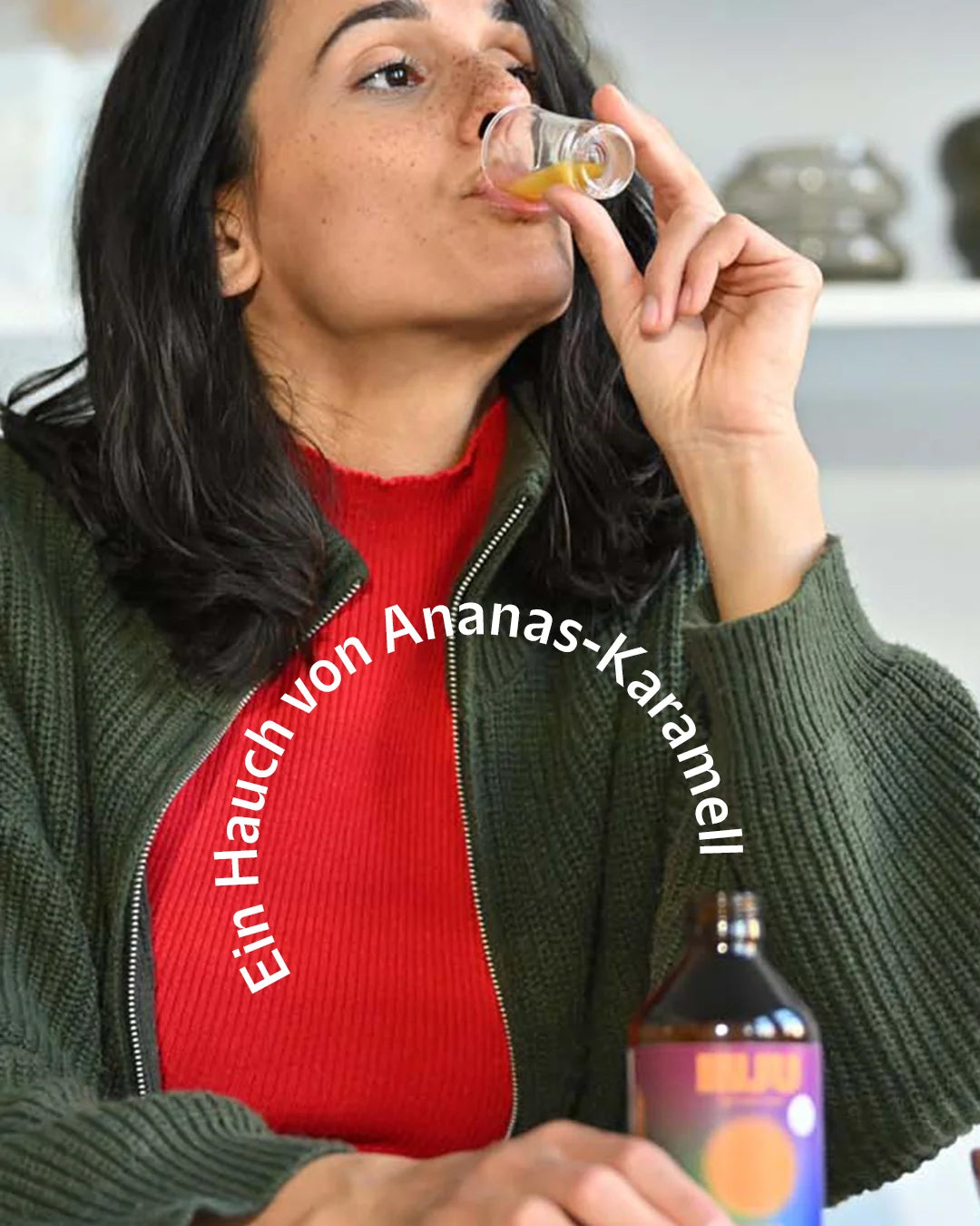 Eine Frau trinkt einen Shot der INJU Immune Essenz. Text-Overlay: „Ein Hauch von Ananas-Karamell“, was auf das Geschmacksprofil des Produkts hinweist.