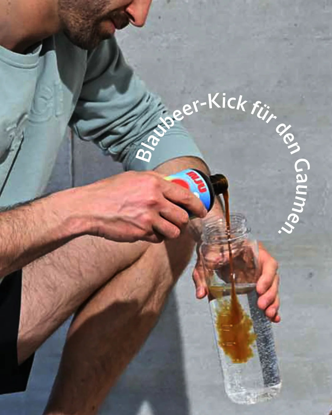 Ein Sportler schenkt die dunkelrote INJU Performance Flüssigkeit in eine Wasserflasche ein. Text-Bogen mit „Blaubeer-Kick für den Gaumen“ .