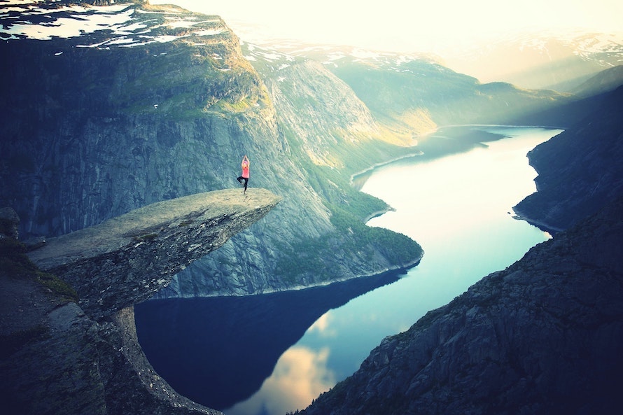 Eine Frau macht Yoga auf einem Felsvorsprung, über einer Bergschlucht mit Fluss
