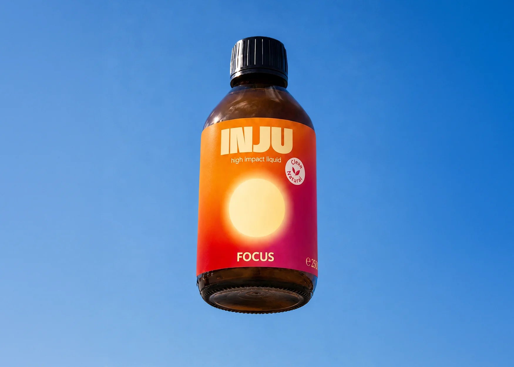 INJU FOCUS-Braunglasflasche vor blauem Himmel. Das orange-rote Etikett zeigt das Logo und einen leuchtend gelben Kreis.