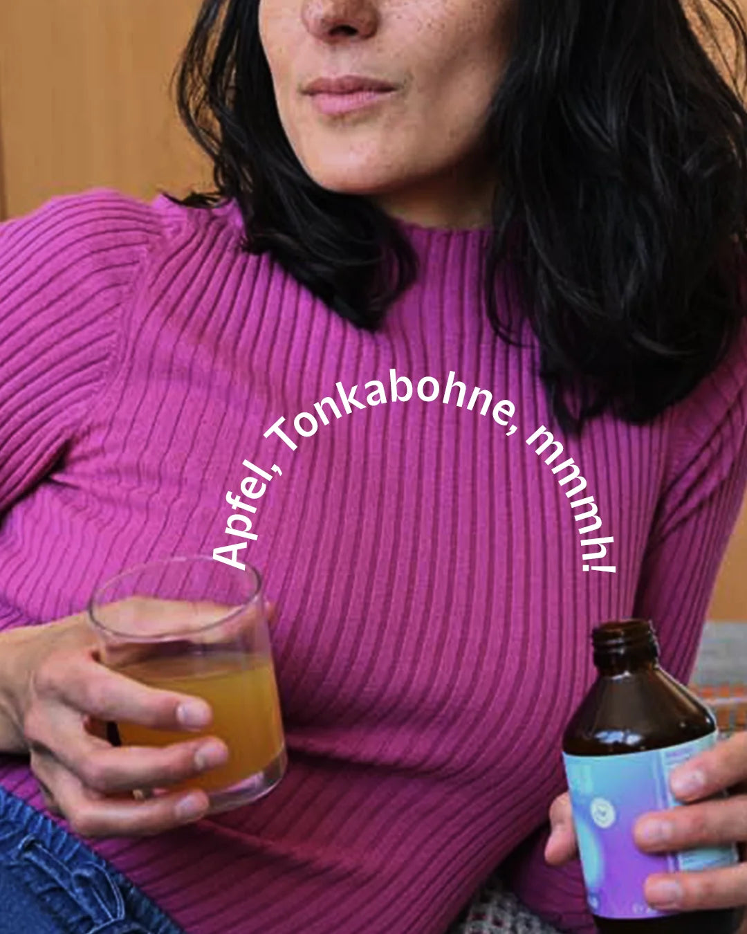 Eine Frau hält ein Glas der goldgelben INJU Calm Essenz. Text-Bogen: „Apfel, Tonkabohne, mmmh!“.