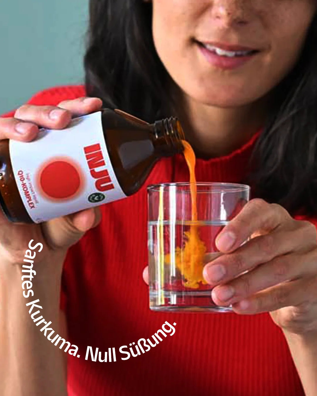Eine Frau gießt die orangefarbene INJU Q10-Essenz aus der Flasche in ein Glas Wasser. Text im Bogen: „Sanftes Kurkuma. Null Süßung.“