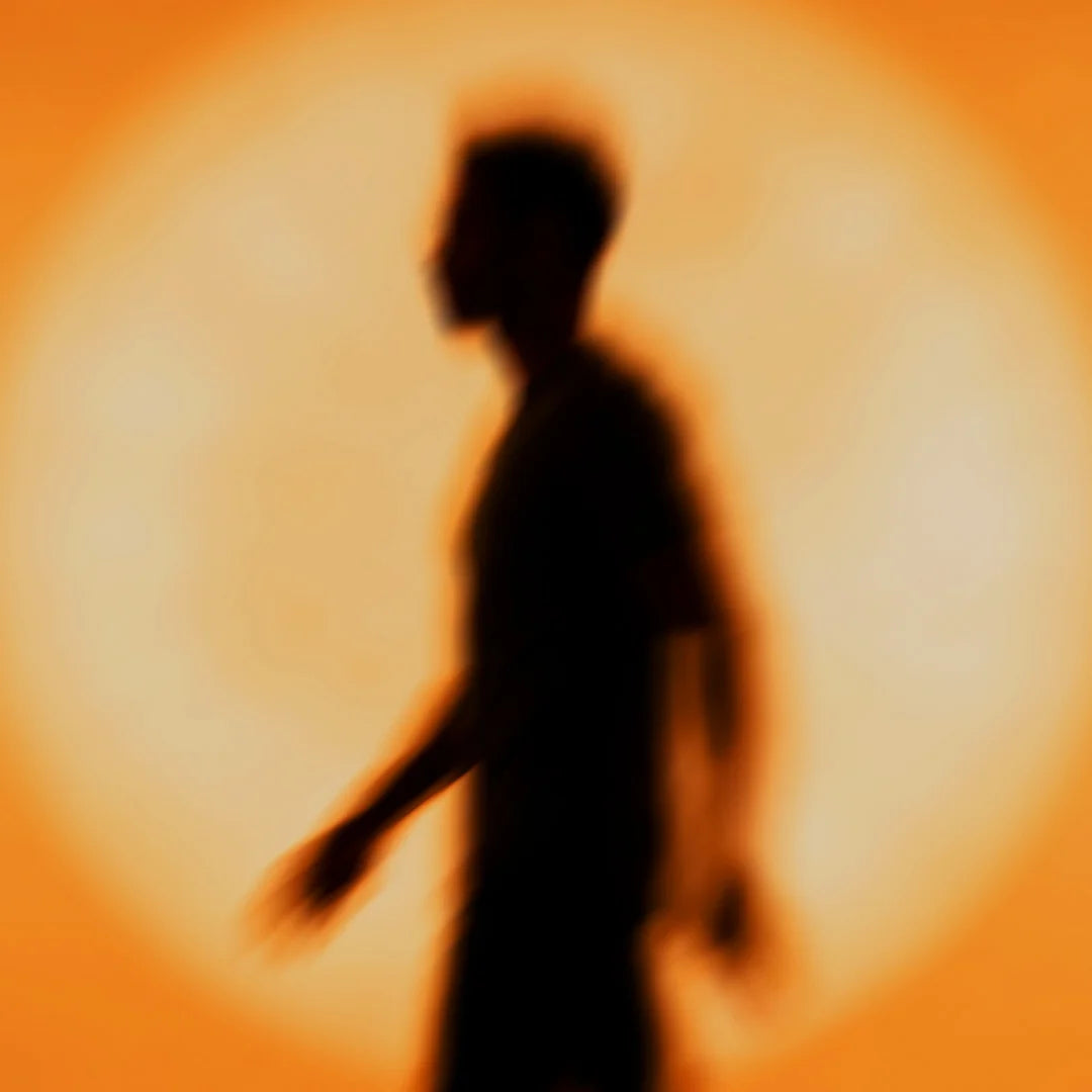 Eine dunkle, verschwommene Silhouette einer gehenden Person im Profil, die zentriert vor einem großen, kreisrunden, hellorange leuchtenden Kreis steht.
